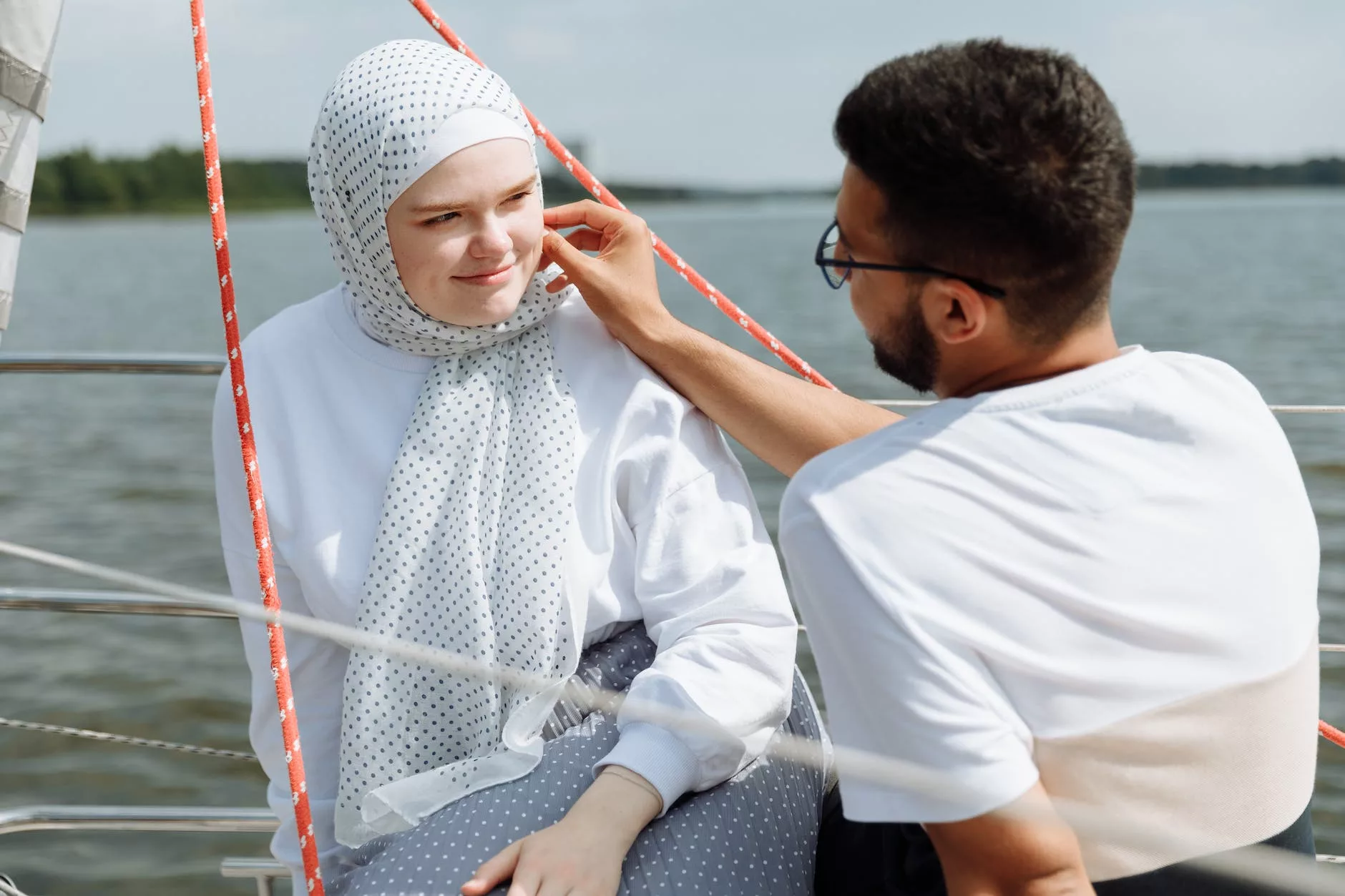man touching the face of a woman in hijab while sitting on a boat